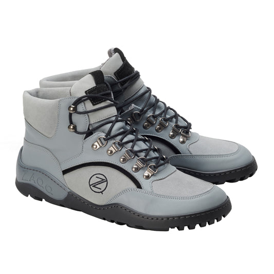 Die TREQ Grey Waterproof Wanderschuhe von ZAQQ sind High-Tops in Grau mit schwarzen Schnürsenkeln, Metallösen und einer robusten schwarzen Gummisohle. Dieser wasserdichte Outdoorschuh trägt ein Logo an der Seite und zeichnet sich durch ein modernes, robustes Design aus, das ideal für Outdoor-Aktivitäten ist.