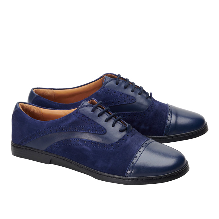 Ein elegantes Paar QENTLE Blue Brogue-Schuhe aus Wildleder und Leder von ZAQQ mit dekorativen Perforationen, ergänzt durch eine schwarze BUSINESS-Sohle und ein hellbraunes Innenfutter. Die Schuhe werden aus einem Winkel präsentiert.