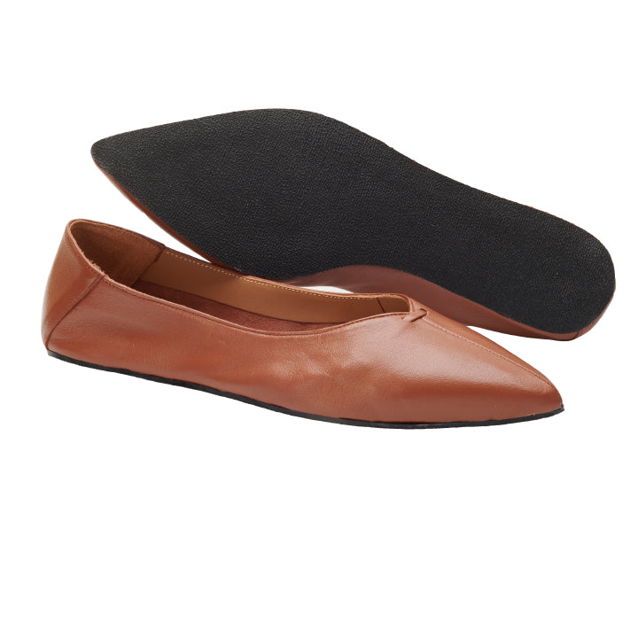 Die MEXIQ Brown von ZAQQ sind braune Leder-Ballerinas mit spitzer Spitze, deren Eleganz an klassische Pumps erinnert. Ein Schuh steht aufrecht, während der andere angewinkelt ist und seine schwarze Sohle freigibt.