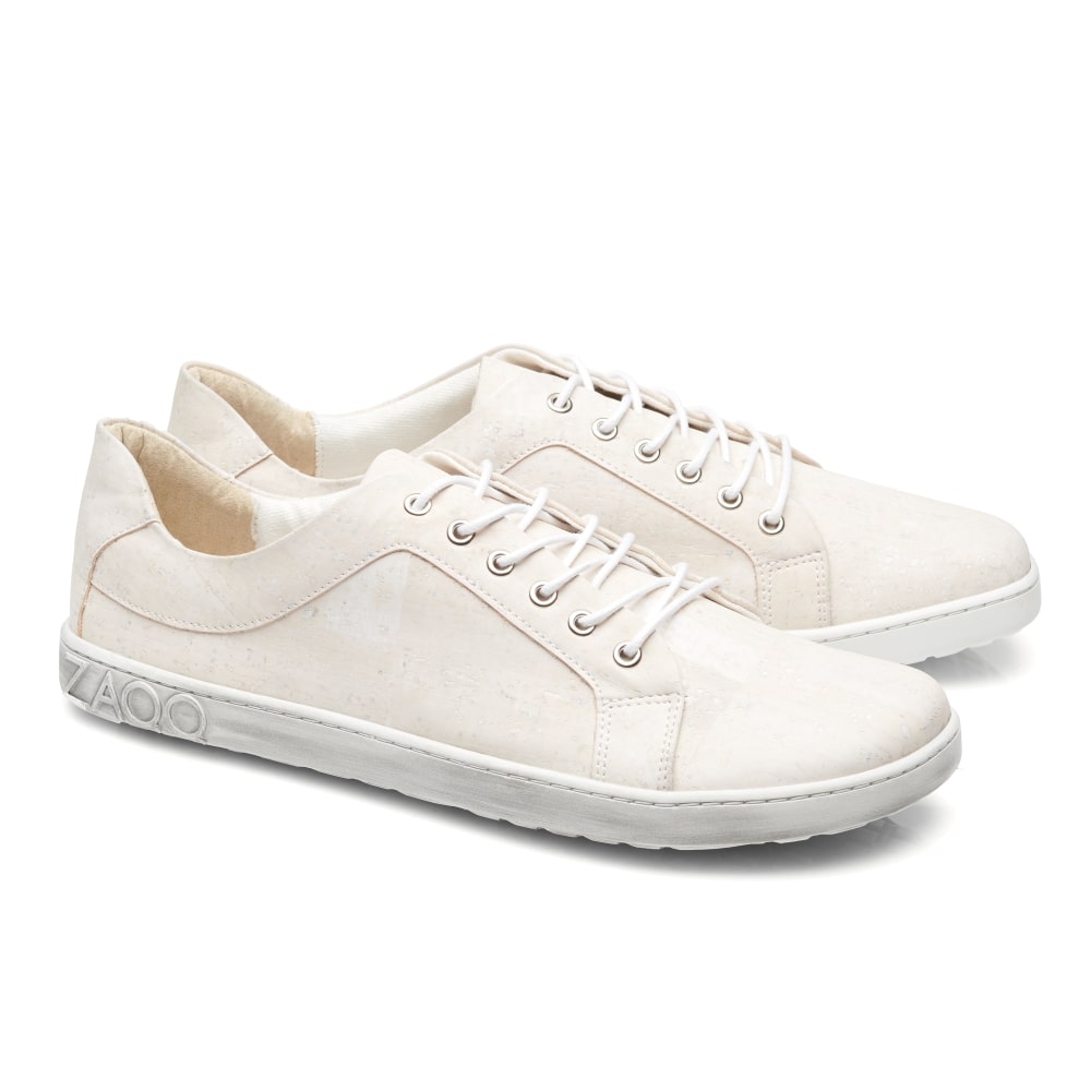 Die QORE Low Vegan White Sneaker von ZAQQ sind cremefarben mit weißen Schnürsenkeln und Sohlen. Diese Schuhe zeichnen sich durch ein minimalistisches Design mit einem subtilen geometrischen Muster auf dem Körper aus und zeigen das Logo der Marke auf der Ferse. Sie werden vor einem schlichten weißen Hintergrund präsentiert.