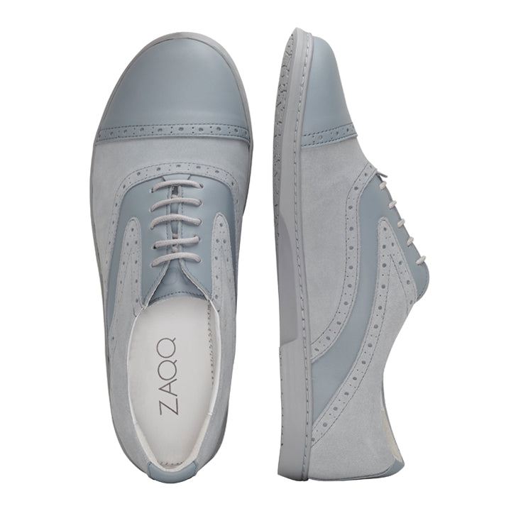 Wir präsentieren den QENTLE Grey von ZAQQ: ein Paar stilvolle Oxford-Schuhe in Grau und Blau, fachmännisch gefertigt aus Velours- und Nappaleder mit Schnürsenkeln. Ein Schuh ist von oben zu sehen und zeigt das markante ZAQQ-Logo auf der Innensohle, während der andere von der Seite betrachtet wird und die aufwendigen Details und das Sohlendesign hervorhebt. Perfekt als Businessschuh für alle, die Wert auf Eleganz legen.