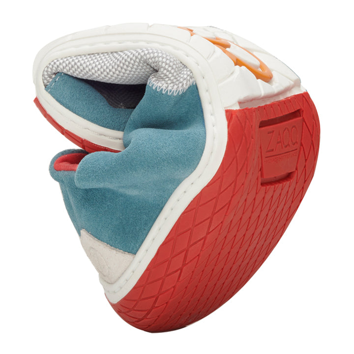 Wir präsentieren den QADIZ Blue Sneaker von ZAQQ: einen flexiblen, gedrehten Schuh mit roter Gummisohle, blauem Wildlederobermaterial, weißen Akzenten und orangefarbenen Details. Dieser Barfußschuh wird gefaltet präsentiert, um seine außergewöhnliche Flexibilität und die markanten Designelemente hervorzuheben.