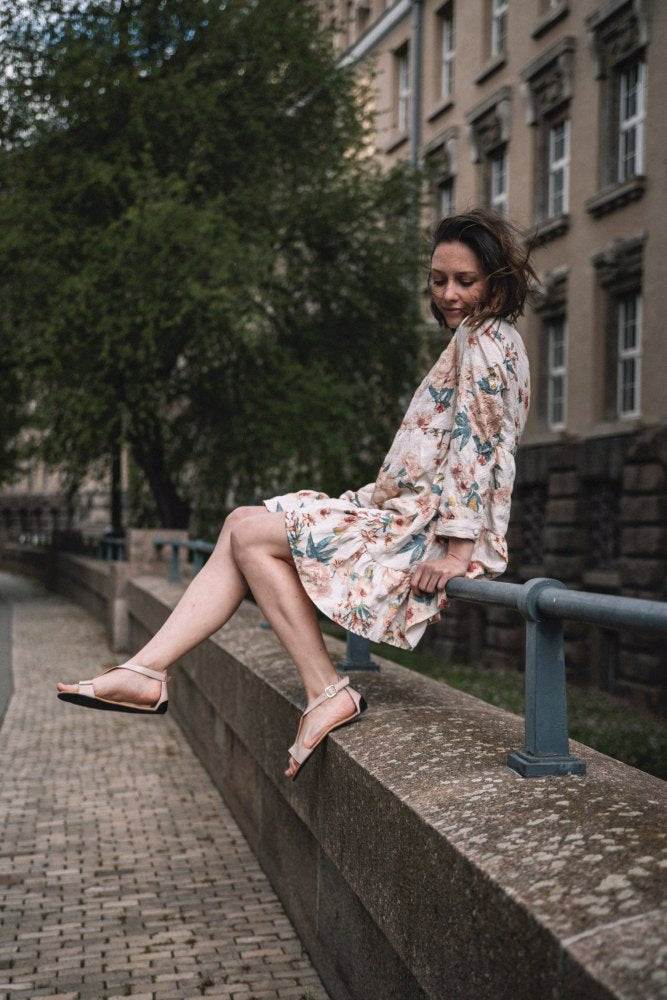 Ein Paar elegante beige Riemchensandalen mit Fesselriemen und flacher Sohle, gefertigt aus weichem Nappaleder, bekannt als CLIQ Beige von ZAQQ.