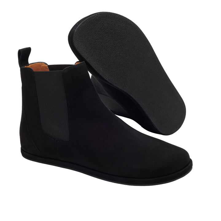 Die EQUITY Velours Black Chelsea Boots von ZAQQ werden kunstvoll präsentiert – ein Stiefel steht aufrecht, während der andere geneigt ist und seine sorgfältig gefertigte Sohle zeigt, wodurch das elegante schwarze Design und die elastischen Seiteneinsätze zur Geltung kommen.