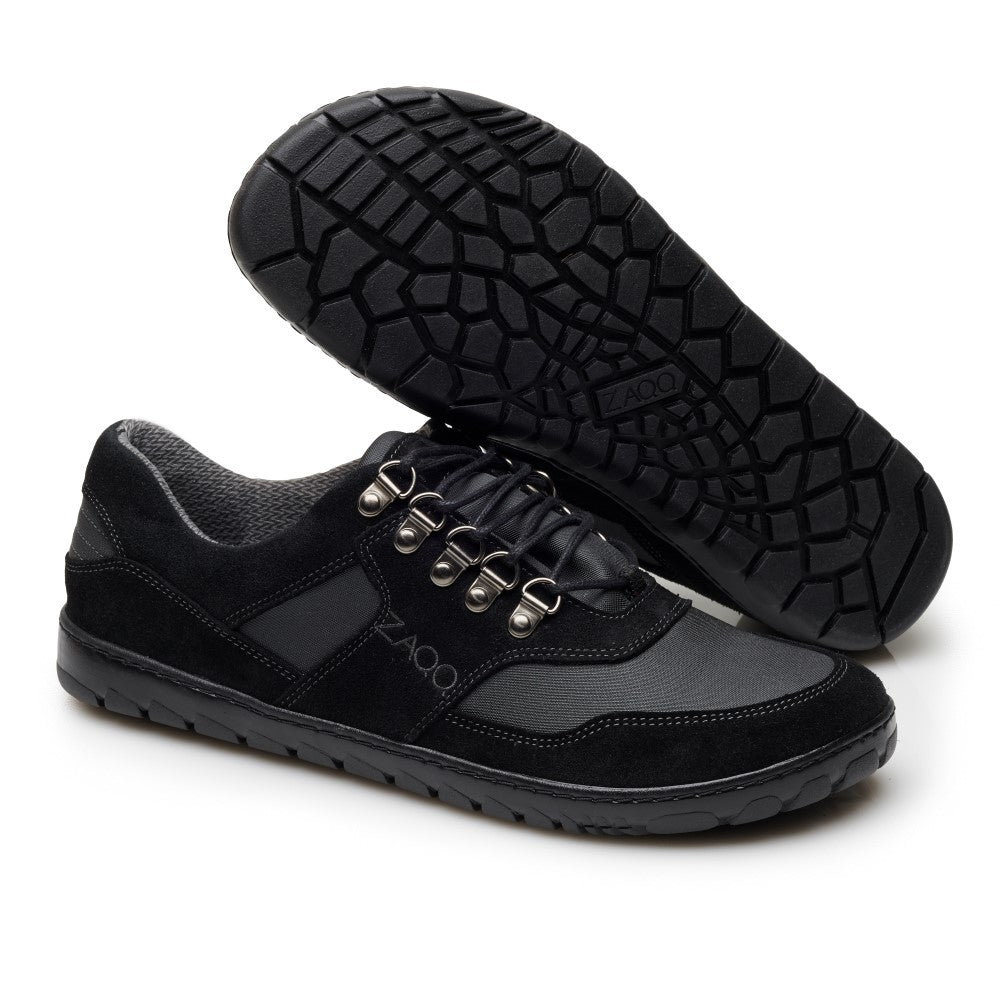 Abgebildet ist ein Paar HIQE Low Black Waterproof-Schuhe von ZAQQ. Diese Schuhe sind mit schwarzen Schnürsenkeln ausgestattet, die durch Metallösen geführt sind, und haben robuste Sohlen, ideal für Outdoor-Aktivitäten. Ein Schuh steht aufrecht, während der andere auf der Seite liegt, wodurch das aufwendige Sohlenmuster hervorgehoben wird, das für optimalen Halt und Haltbarkeit gefertigt wurde.