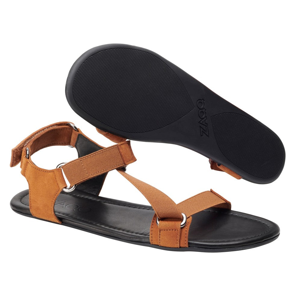 Die MIQA Brown Sandalen von ZAQQ sind aus hochwertigem Veloursleder gefertigt und verfügen über eine schwarze Sohle, ein verstellbares Riemchensystem und Metallringe zur Befestigung. Eine Sandale wird flach präsentiert, während die andere aufrecht steht, um das Sohlendesign hervorzuheben.