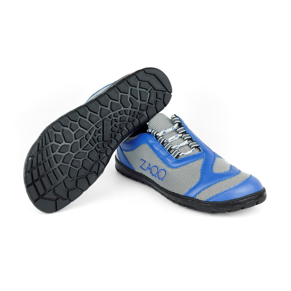 Die Sportschuhe ZAQQ QUIQ Trail Blue zeichnen sich durch ein auffälliges blau-graues Design aus, wobei ein Schuh aufrecht steht, während der andere geneigt ist, um die schwarze Sohle mit sechseckigem Muster zu zeigen. Diese Barfußschuhe sind aus Meshgewebe für hervorragende Atmungsaktivität gefertigt und bieten unvergleichlichen Komfort und Stil.