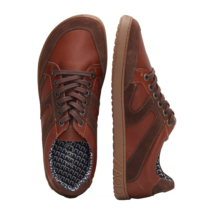 RIQO Brown von ZAQQ bietet stilvolle braune Freizeitschuhe mit strukturierter Oberfläche, braunen Schnürsenkeln und einem gemusterten Innenfutter für außergewöhnlichen Tragekomfort. Ein Schuh liegt flach, während der andere aufrecht steht, um das Seitenprofil dieser modischen und dennoch atmungsaktiven Schuhe zu präsentieren.