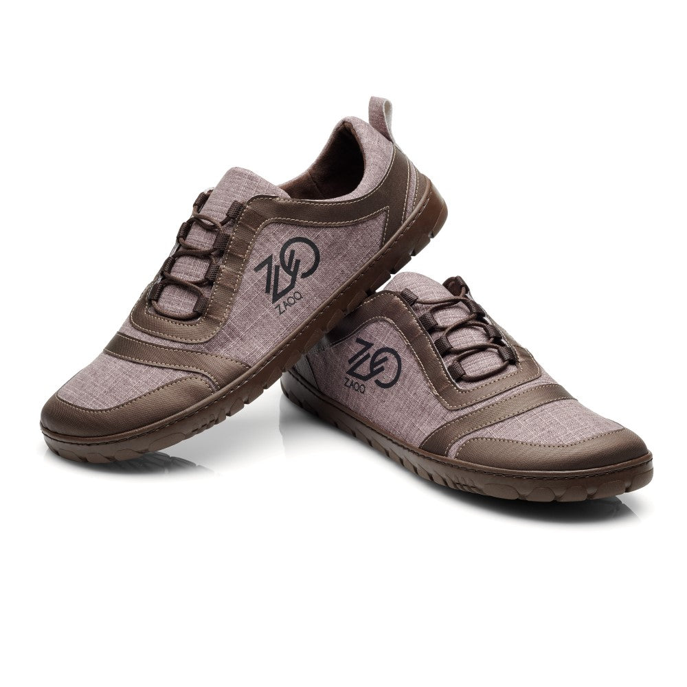 Ein Paar SQILL Brown Casual Sneakers von ZAQQ mit Schnürdesign und dunkelbraunen Akzenten. Diese Sneakers aus veganem Obermaterial zeigen ein stilisiertes Logo an der Seite. Sie sind auf einem schlichten weißen Hintergrund abgebildet, wobei ein Schuh an den anderen lehnt.