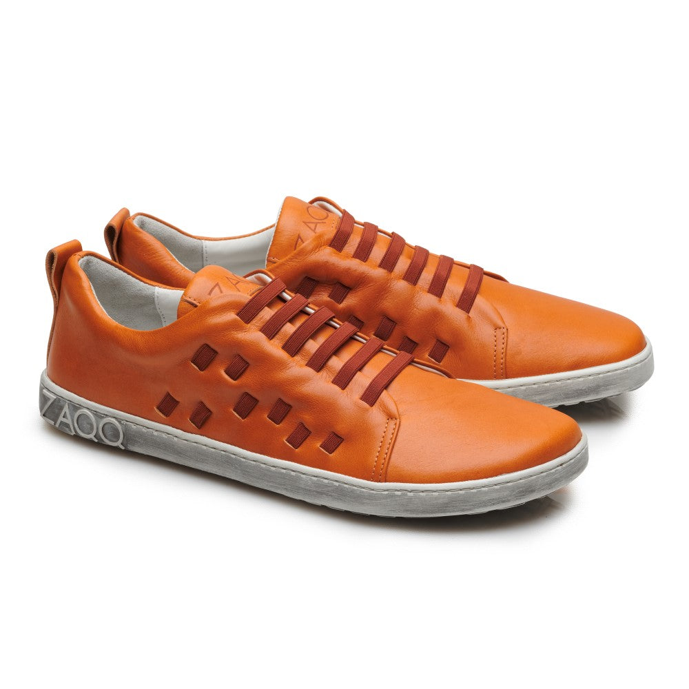 Wir präsentieren den STRAQ Sierra von ZAQQ: ein Paar stylische orangefarbene Sneaker aus Nappaleder mit weißer Sohle. Die Seiten sind mit quadratischen Ausschnittmustern versehen und der Markenname ZAQQ ist elegant auf der Ferse eingeprägt. Diese Barfuß-Sneaker zeichnen sich durch ein Schnürdesign mit braunen Schnürsenkeln aus.