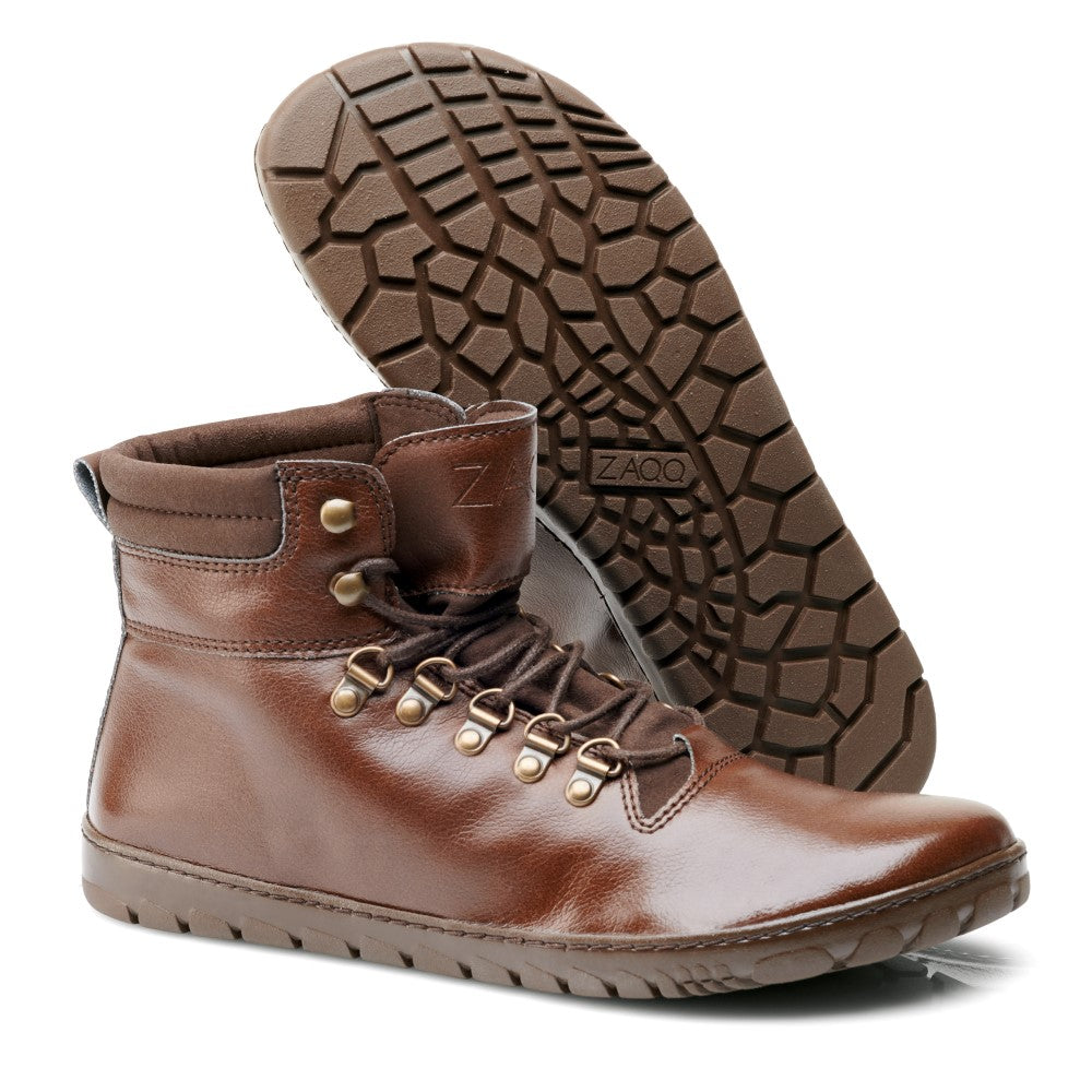 Die EXPEQ Vegan Marone Waterproof-Stiefel von ZAQQ haben ein glänzendes braunes Finish mit einem praktischen seitlichen Reißverschluss und Messingösen, gepaart mit dunkelbraunen Schnürsenkeln. Sie sind mit einer geometrisch gemusterten, dicken, rutschfesten Gummisohle in Braun gestaltet. Ein Stiefel steht aufrecht, während der andere auf der Seite liegt, was ihren Outdoorschuh-Charakter unterstreicht.