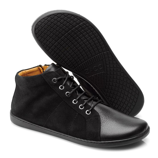 Die ZAQQ QORE Mid Black High-Tops bestehen aus einer Mischung aus Leder und Wildleder, ergänzt durch silberne Ösen und elegante schwarze Schnürsenkel. Ein Schuh steht aufrecht, während der andere seine strukturierte Sohle zeigt und so den minimalistischen Charme dieses Sneakers einfängt.