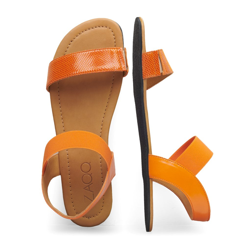 Die SLIQ-Orange-Sandalen von ZAQQ haben breite Riemen. Eine Sandale liegt flach und zeigt die Innensohle mit dem ZAQQ-Logo, während die andere aufrecht steht und das modische Sohlen- und Riemendesign zur Schau stellt.