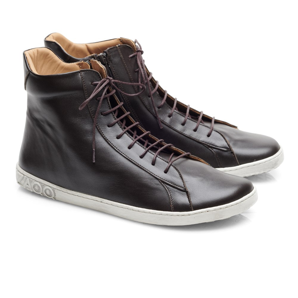 Ein Paar elegante, dunkelbraune SNAQ High-Top-Sneaker von ZAQQ mit weißen Gummisohlen und braunen Schnürsenkeln. Die Schuhe sind abgewinkelt, um die Seiten hervorzuheben, und haben eine leicht erhöhte Rückseite, mit einem beigefarbenen Innenfutter, das einen Hauch von Kontrast verleiht.