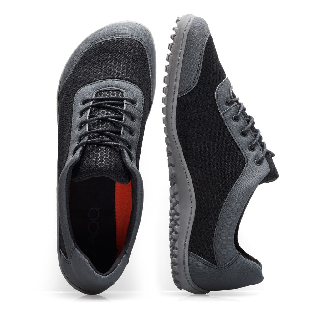 Die ZAQQ SQIP Black Grey sind dunkelgraue, lässige vegane Sneaker mit schwarzem Mesh-Gewebe und grauen Gummisohlen. Ein Schuh steht aufrecht, der andere ist vertikal mit der Oberseite nach vorne positioniert, um das Schnürdesign und die strukturierte Sohle für optimalen Komfort hervorzuheben.